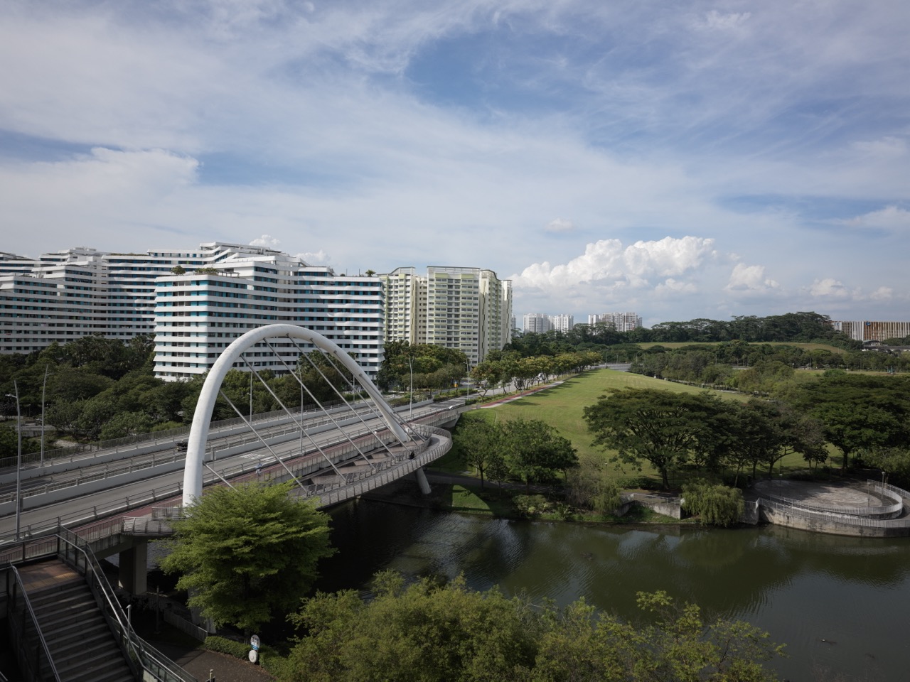 An elevated view shows a white arch bridge carrying a road across a waterway in Punggol, with landscaped greenery and apartment blocks around it.