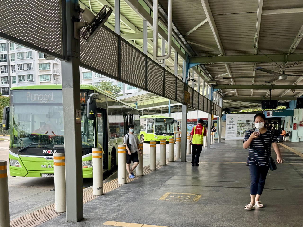 Bus passengers alighting at Punggol Temporary Bus Terminal while one commuter looks at a phone.