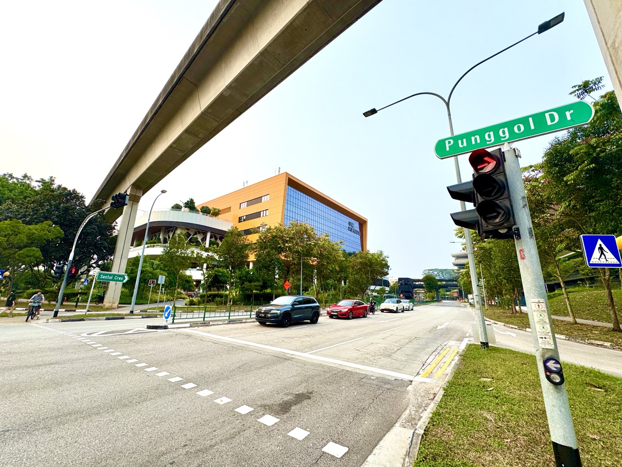 Punggol Drive beneath elevated LRT tracks with the One Punggol community hub in the background.