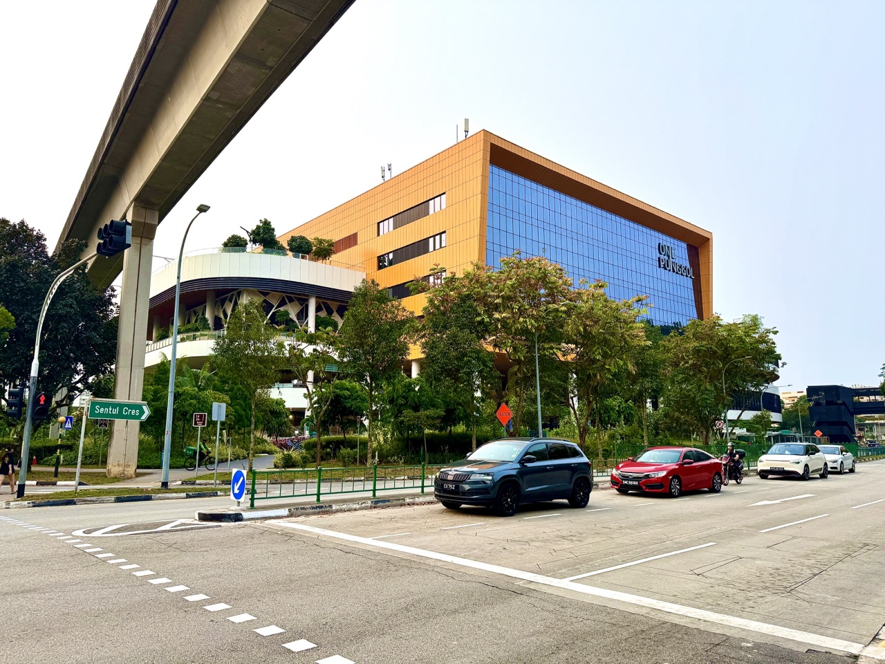 Cars stopped at a Punggol Drive traffic junction beneath elevated LRT tracks, with One Punggol behind.