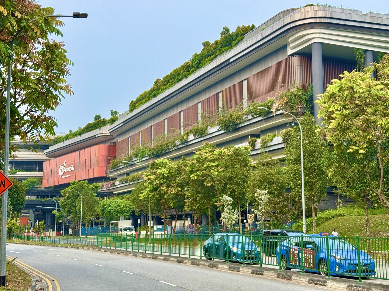 Exterior of Punggol Regional Sport Centre with taxis and a cart on the nearby road.