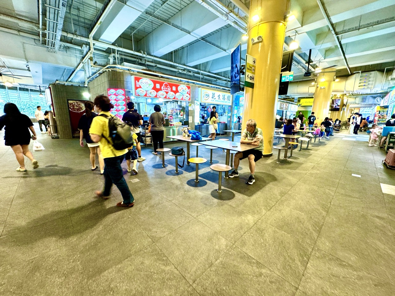 People walking, ordering food and dining at tables in One Punggol Hawker Centre.