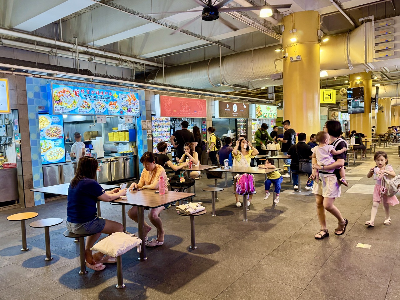 Customers queuing at One Punggol Hawker Centre while food-delivery workers collect orders.
