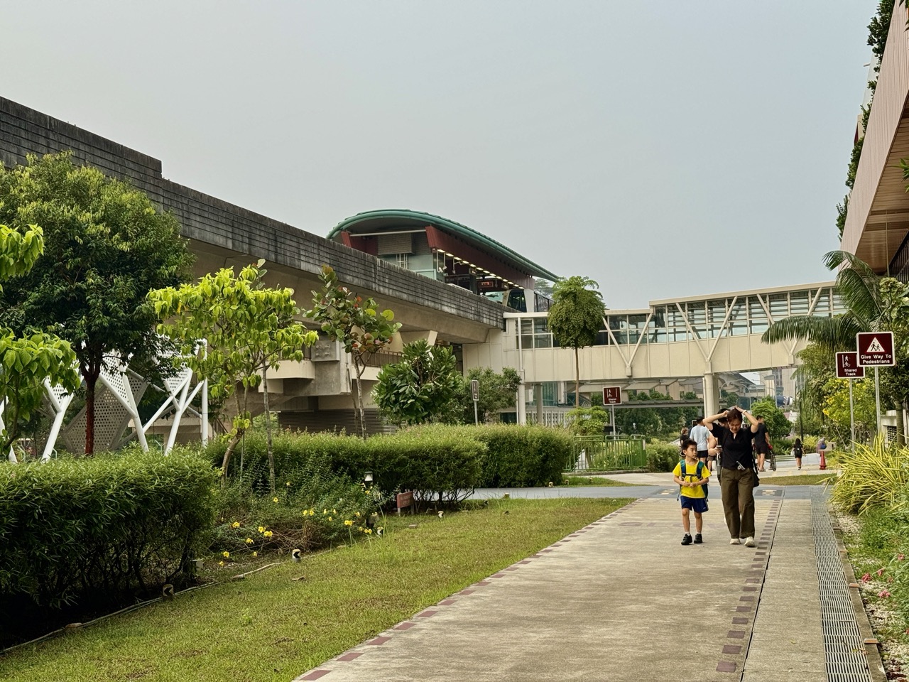 Man walking with a child on a shared path beside elevated Sam Kee LRT tracks.