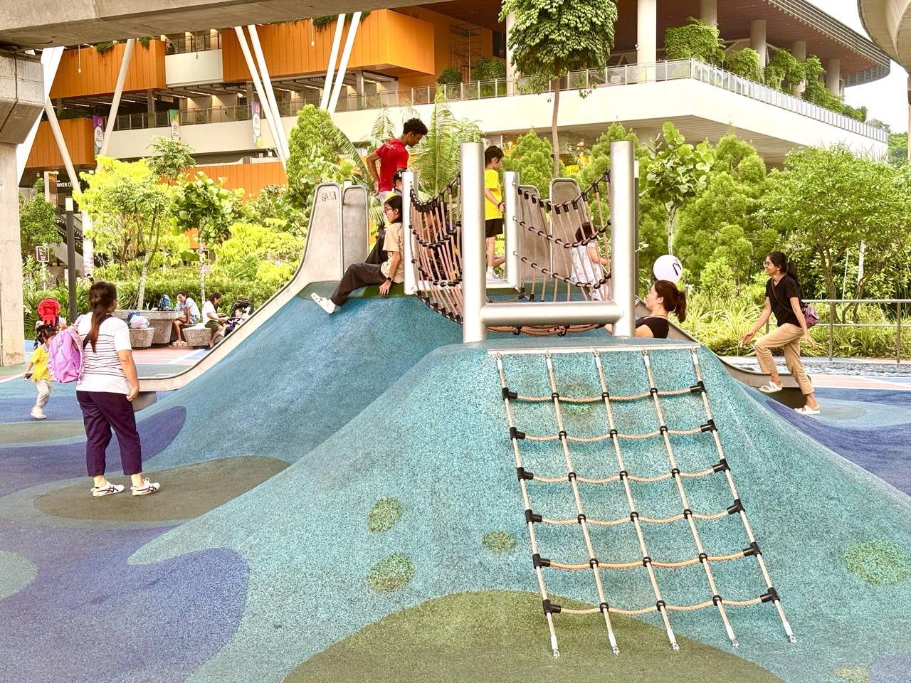 Children and parents using a playground beneath elevated Punggol LRT tracks.